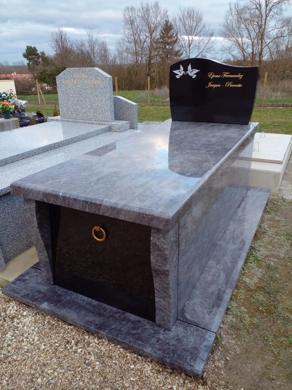 Monument funéraire massif en granit bleu et stèle en marbre noir gravée de colombes blanches