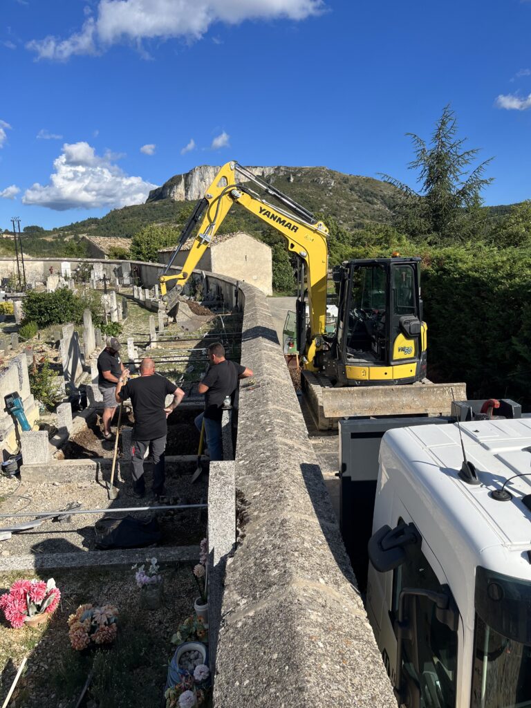 Équipe de marbriers qualifiés pose et installe un monument avec une mini-pelle dans un cimetière